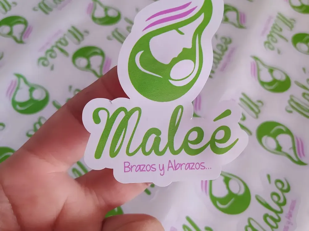 Sticker troquelado personalizado sostenido frente a una plancha impresa